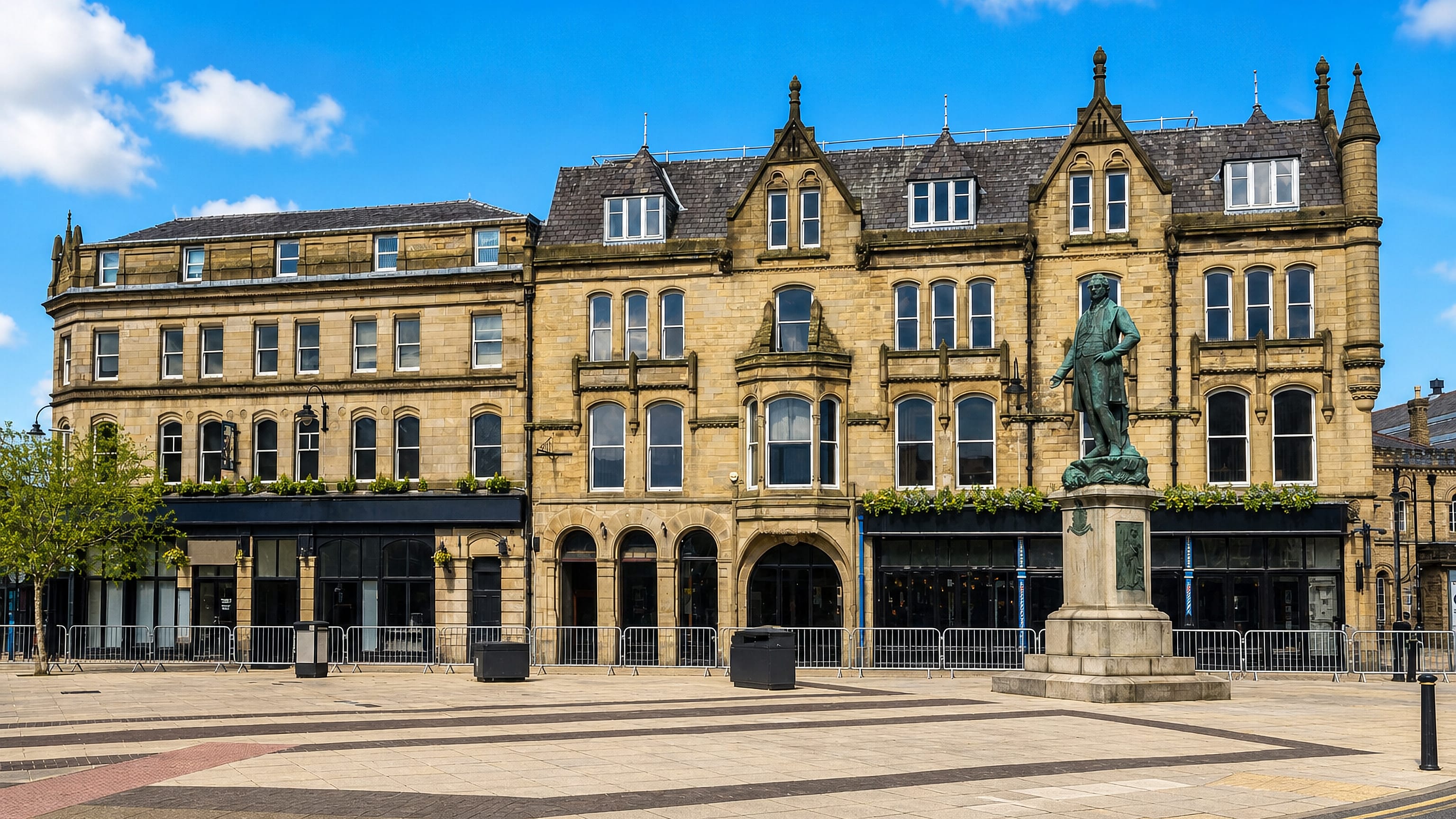Bury town centre square in England, with a bronze statue on a stone plinth before Victorian sandstone buildings.