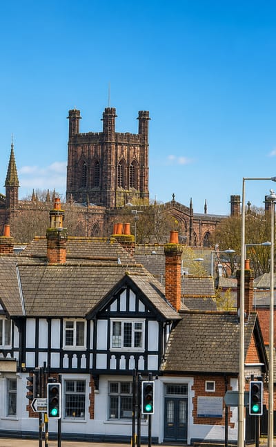 Chester Cathedral's sandstone tower rising above a black-and-white Tudor building on a sunny city street