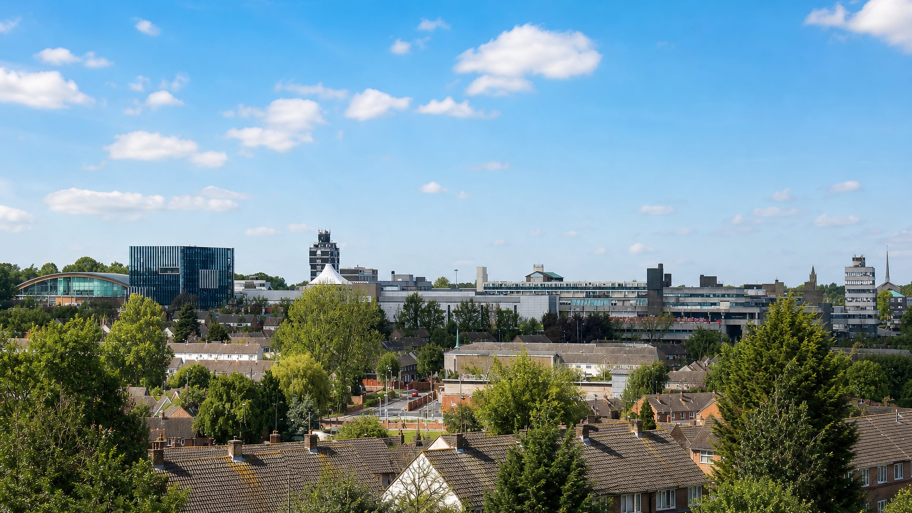 Housing rooftops and mature trees below the modern town-centre buildings of Corby, Northamptonshire, England.