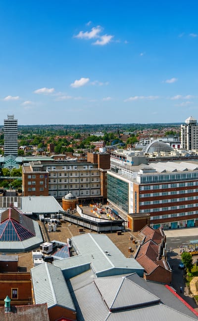 Coventry city centre rooftops beneath the tall Gothic cathedral spire under a bright blue sky