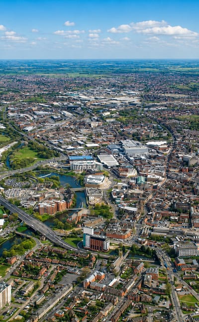 Aerial view of Derby, the River Derwent winding past mixed housing, industry and a ring road under blue sky