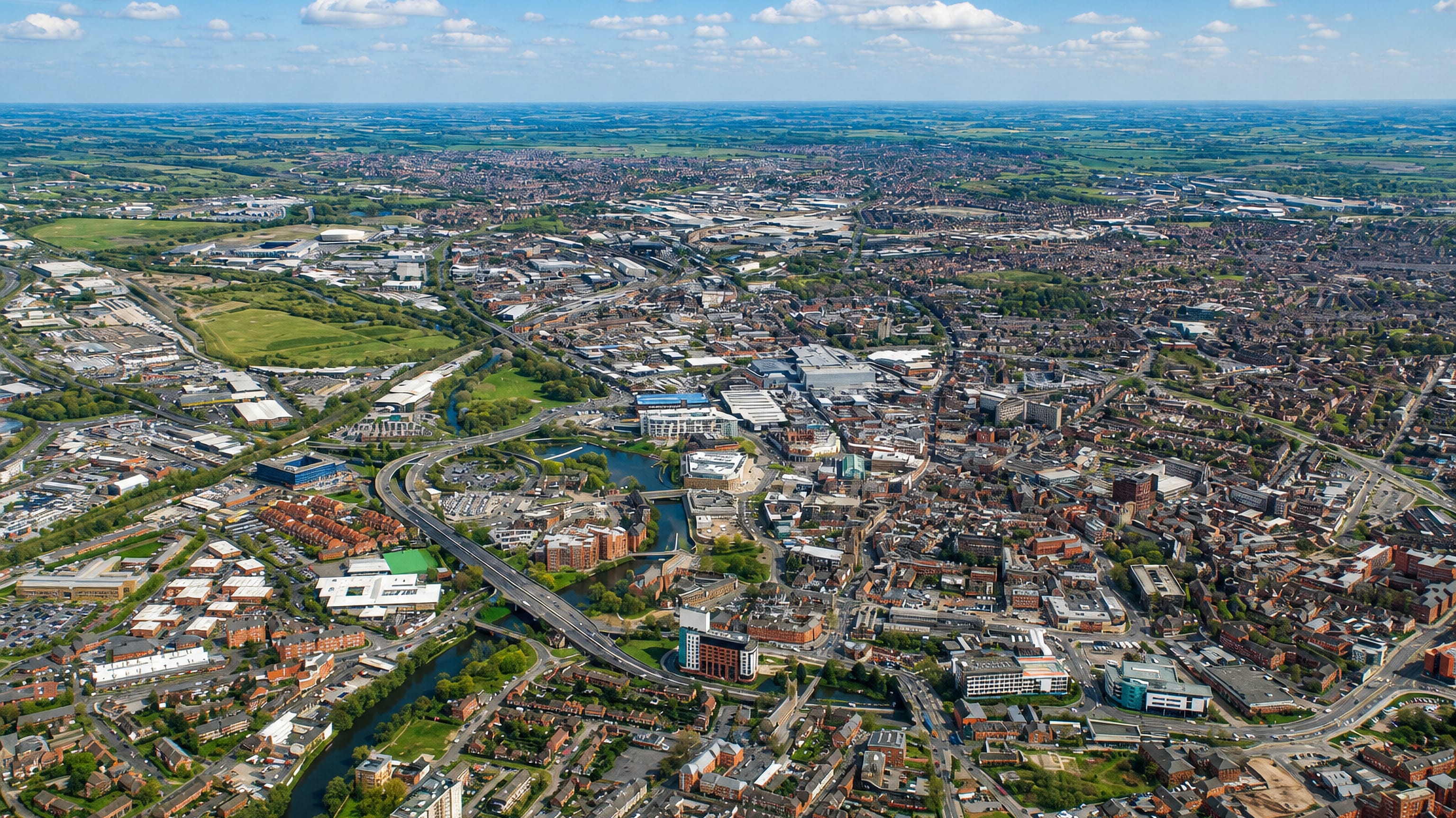 Aerial view of Derby, the River Derwent winding past mixed housing, industry and a ring road under blue sky