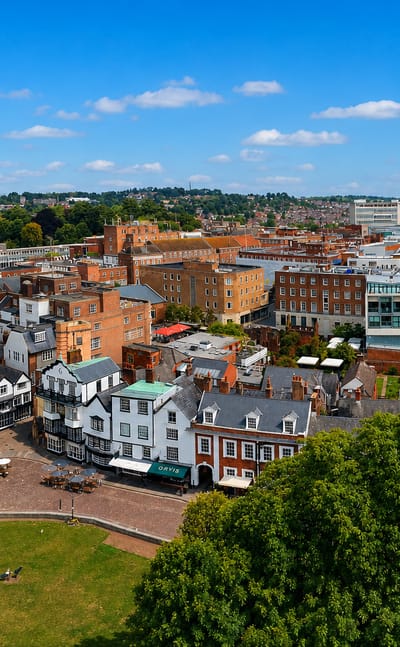Aerial view over Exeter's historic city centre, with timbered buildings, red-brick terraces and a church spire