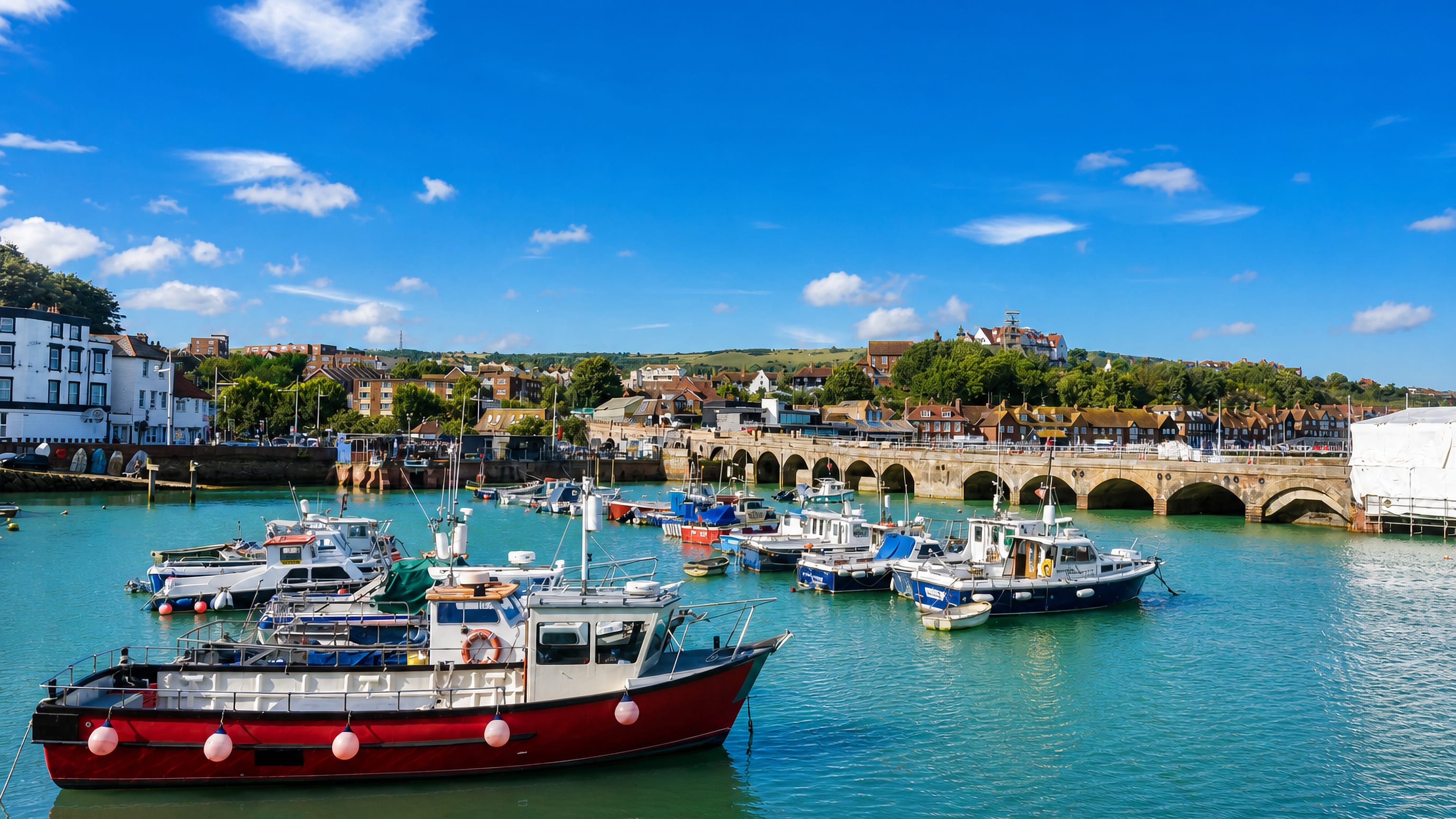 Fishing boats moored in Folkestone harbour below the arched railway viaduct and the town rising on the hillside.