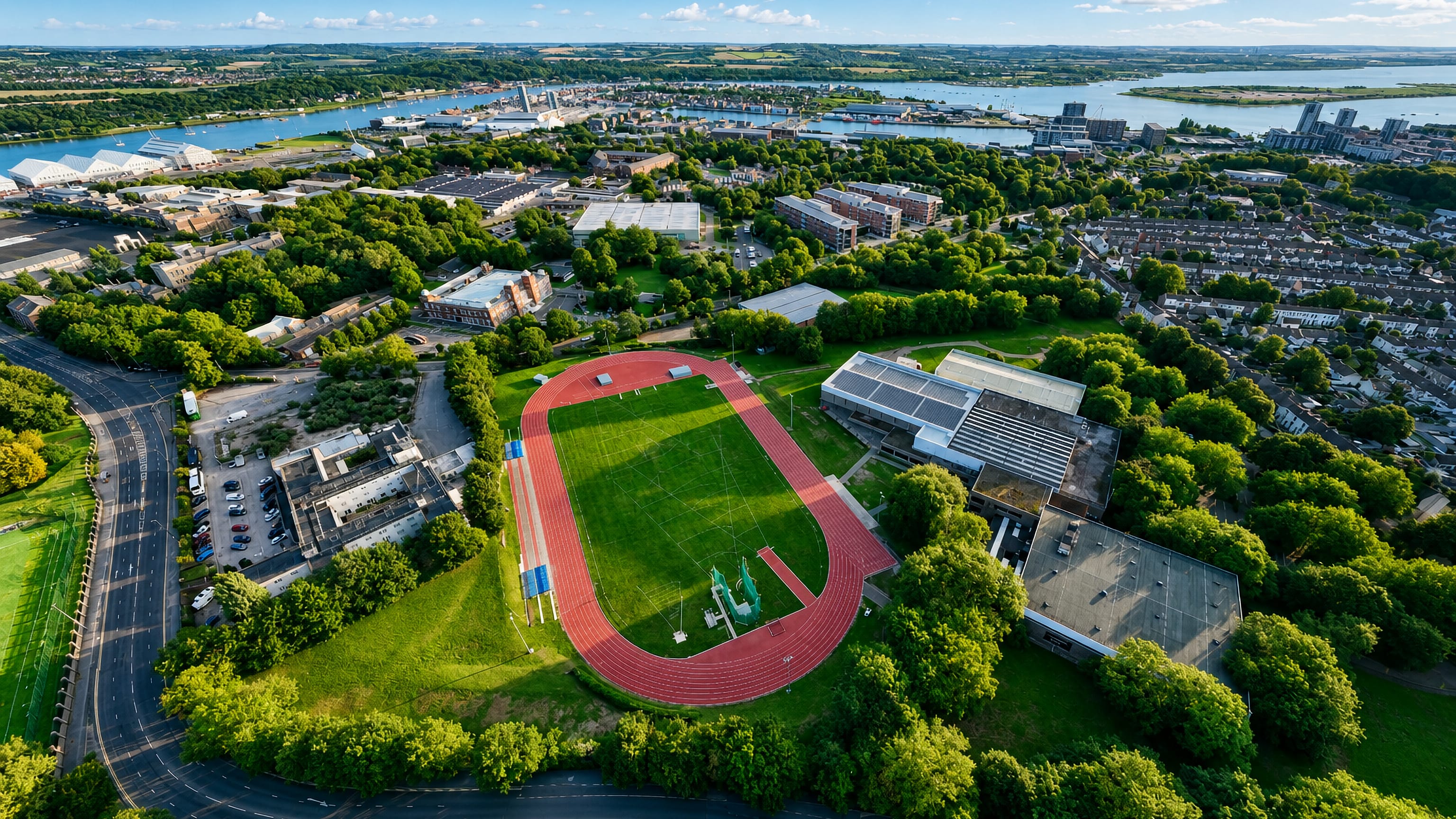 Aerial view over Gillingham, Kent, with an athletics track, leafy streets and the River Medway estuary behind.