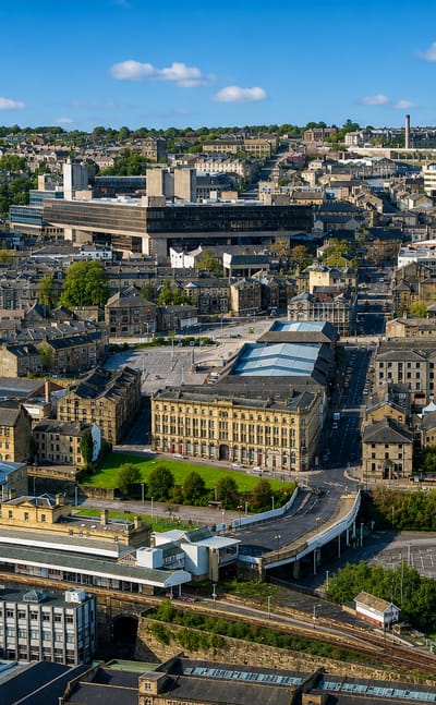 Aerial view of Halifax with its stone mill-town buildings, church spire and wooded hills.