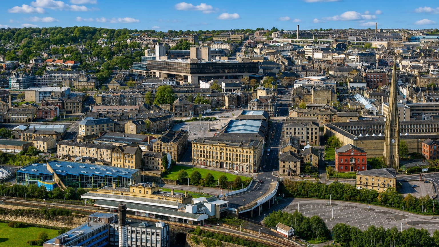 Aerial view of Halifax with its stone mill-town buildings, church spire and wooded hills.