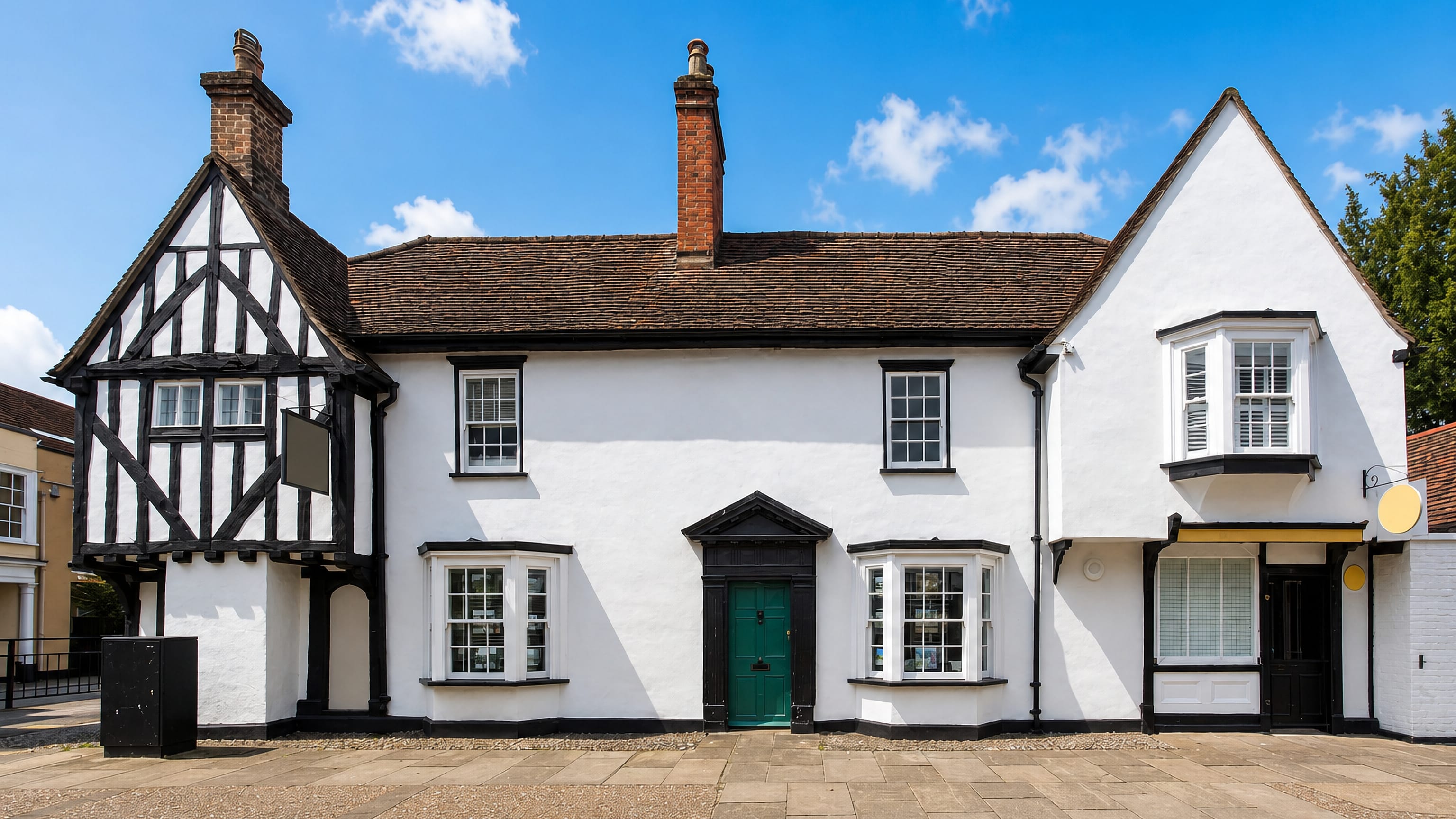 A white-rendered, part timber-framed historic house on a paved square in Harlow, Essex, England.