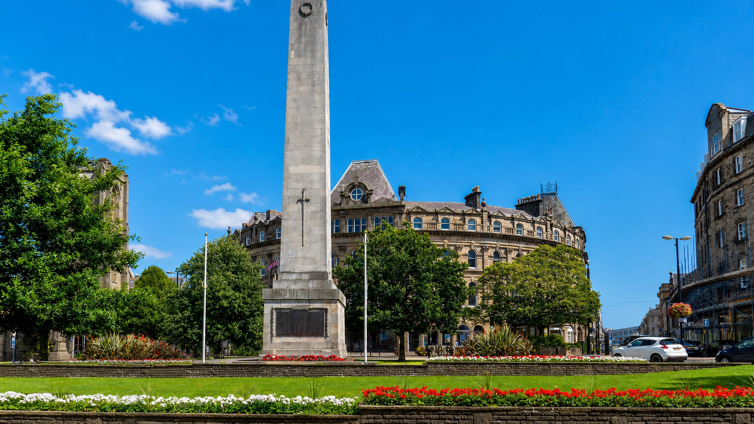 Harrogate's war memorial obelisk on Prospect Square, backed by curved Victorian sandstone terraces and flowerbeds.