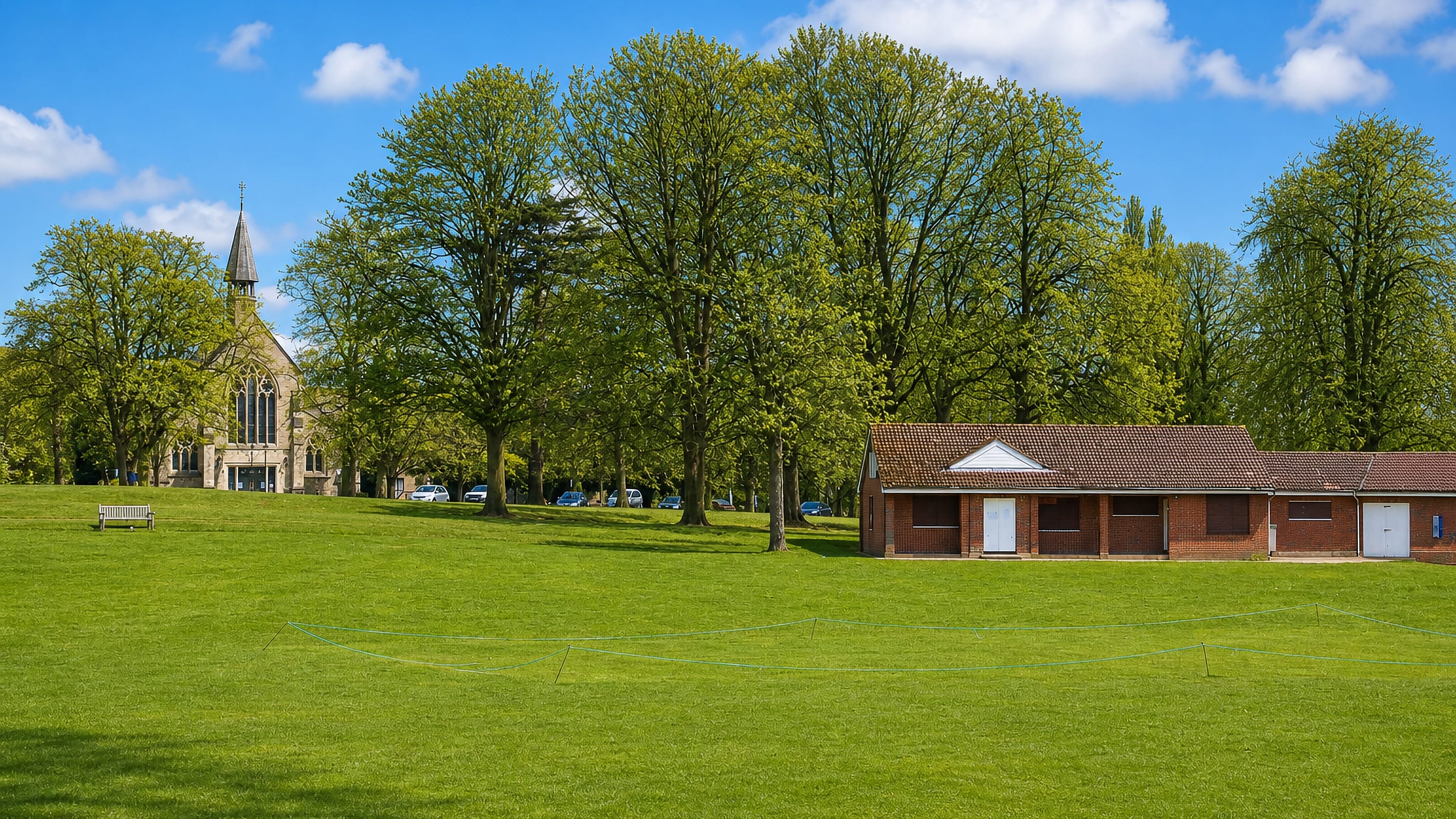 Open green common at Boxmoor, Hemel Hempstead, with a stone church spire and brick cricket pavilion among trees.
