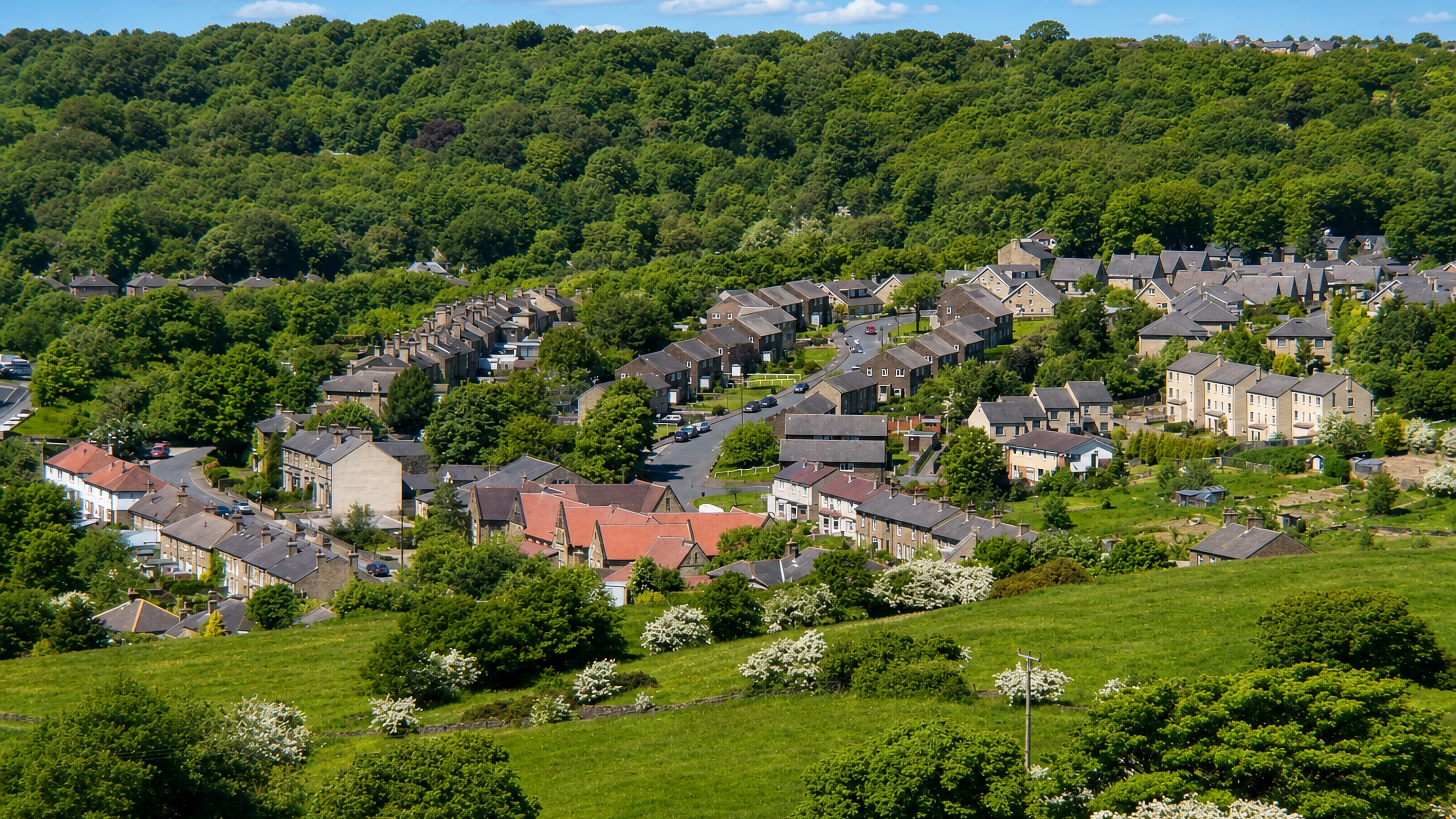 Stone terraces and slate roofs stepping down a wooded Pennine valley at Berry Brow, Huddersfield.
