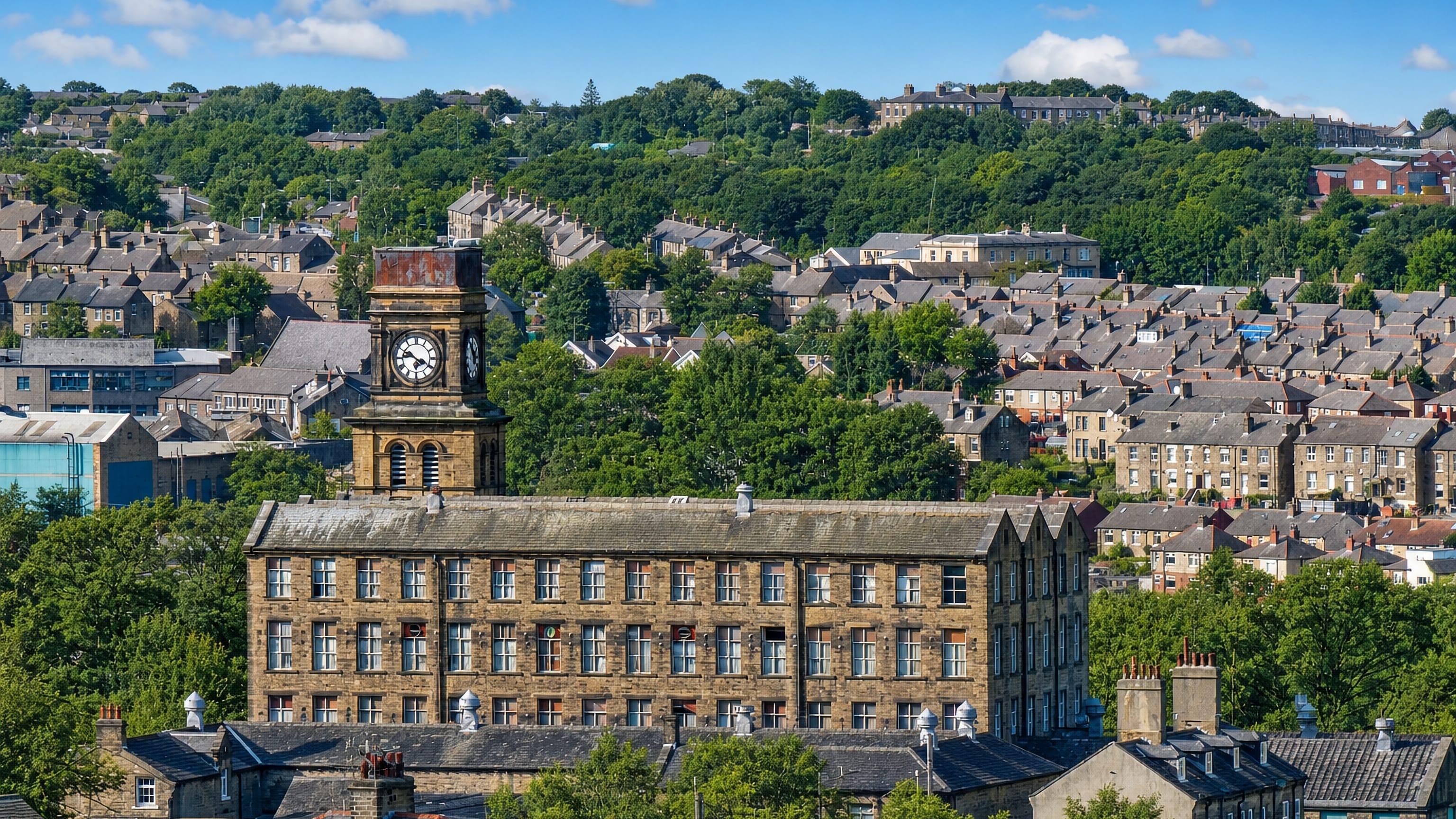 Stone terraced houses, a mill clock tower and wooded hillsides in Huddersfield, West Yorkshire.