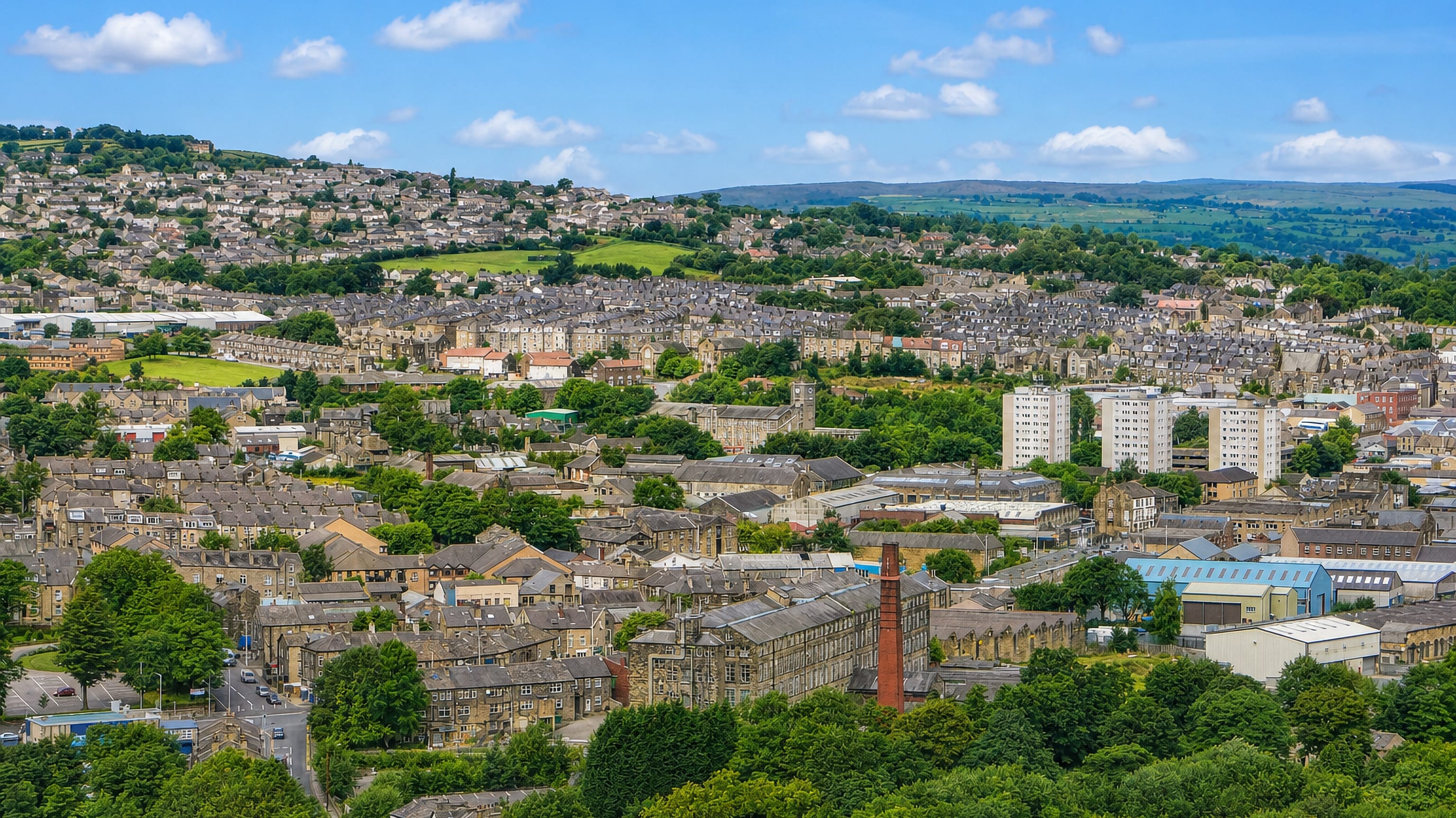 Stone terraces, a mill chimney and tower blocks in Keighley, West Yorkshire, below green Airedale hillsides.