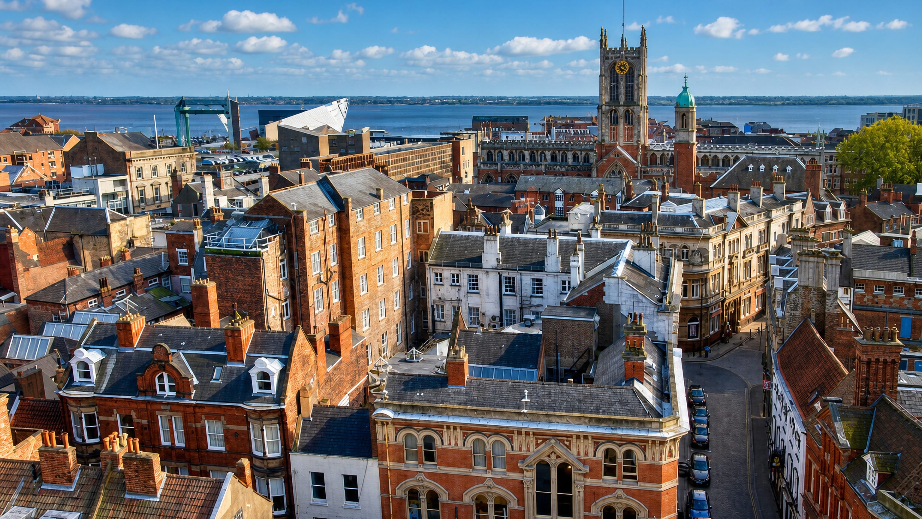 Rooftops of Kingston upon Hull's old town with Hull Minster's tower and the Humber estuary beyond.