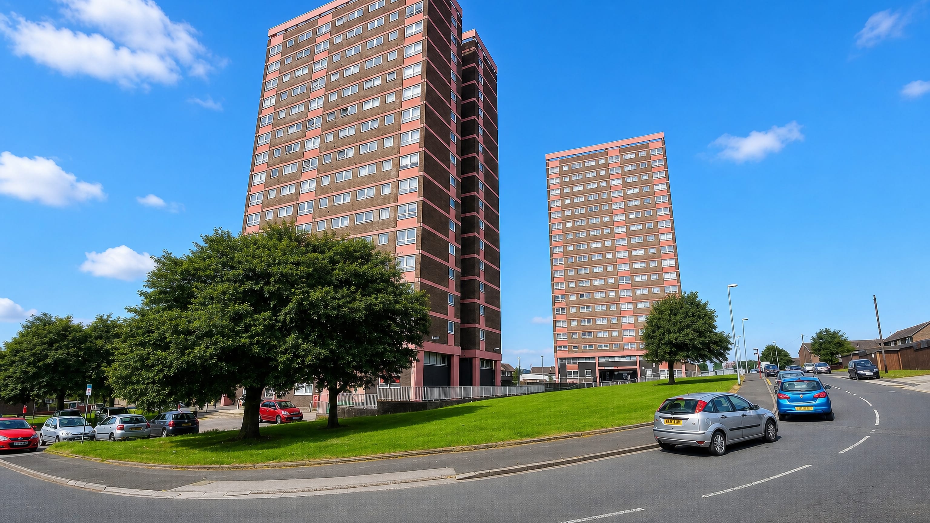 Pink-clad residential tower blocks above a grass verge and quiet road in Bramley, Leeds.