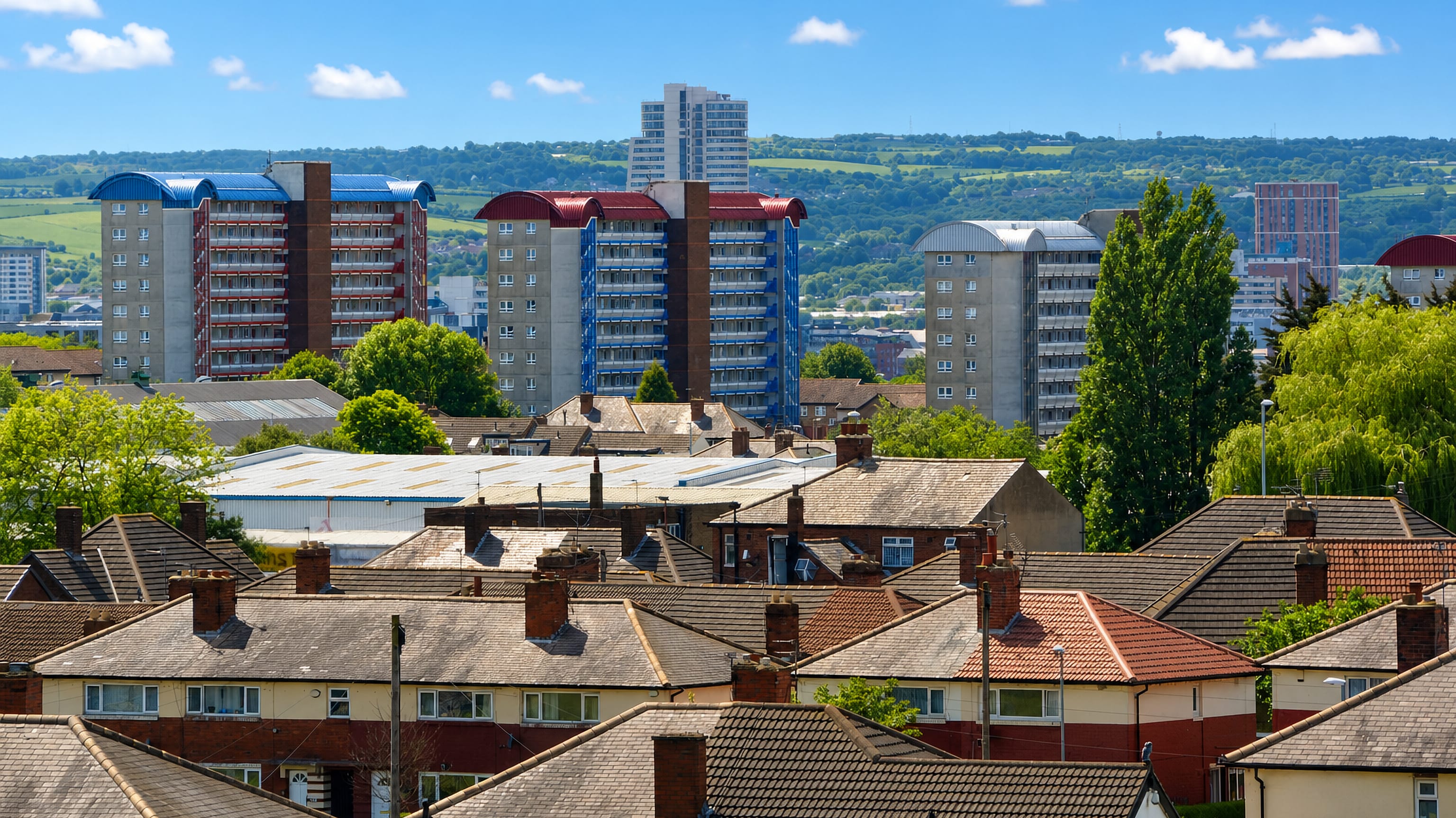 Colour-topped tower blocks above terraced rooftops in Burmantofts, Leeds, with green hills beyond.