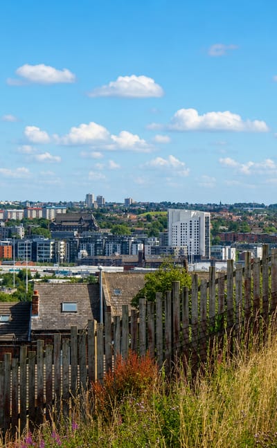 Leeds skyline of apartment towers and brick terraces seen across rooftops from a grassy hillside