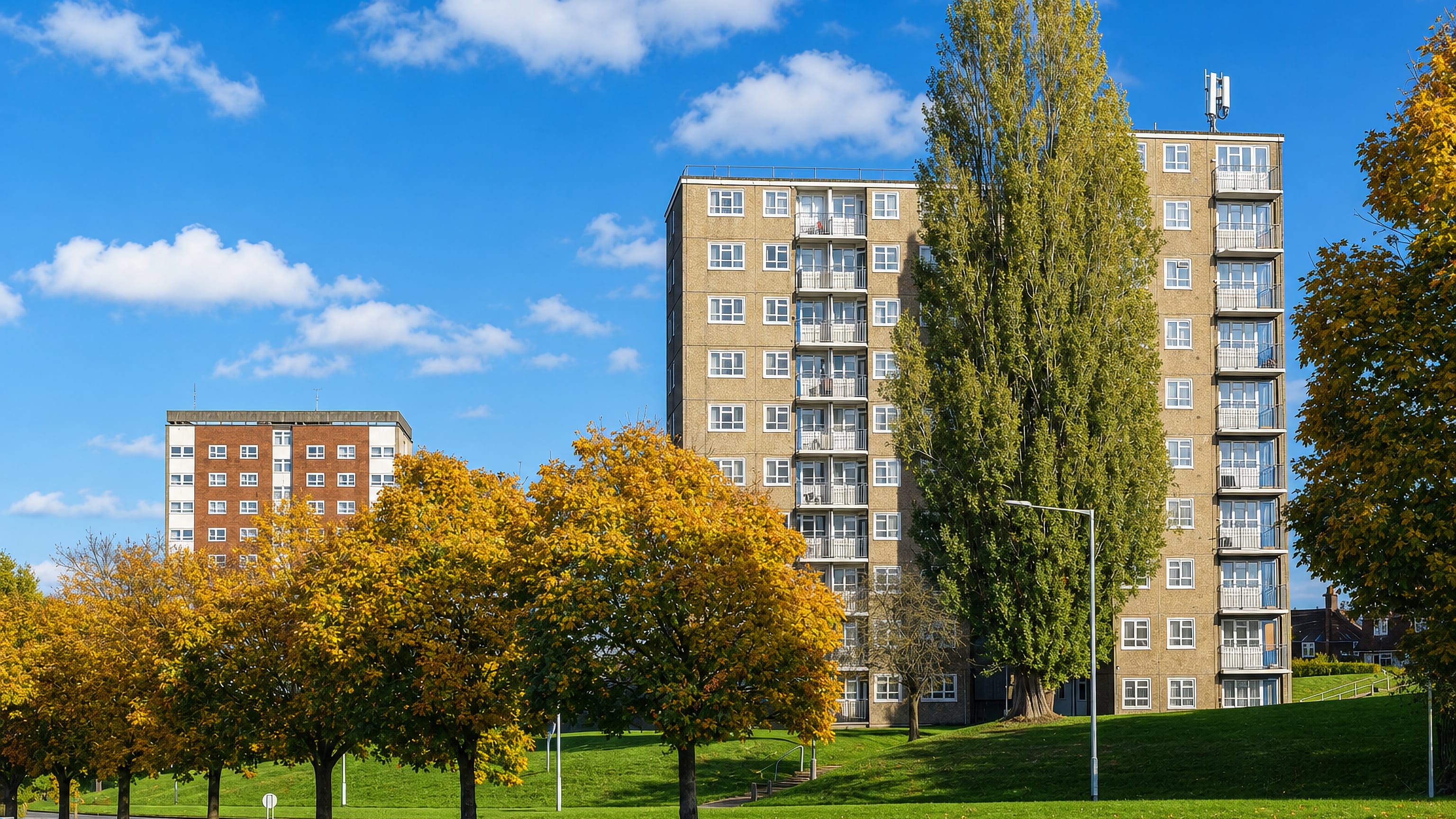 Brick and concrete tower blocks above autumn trees and lawns in Gipton, Leeds.