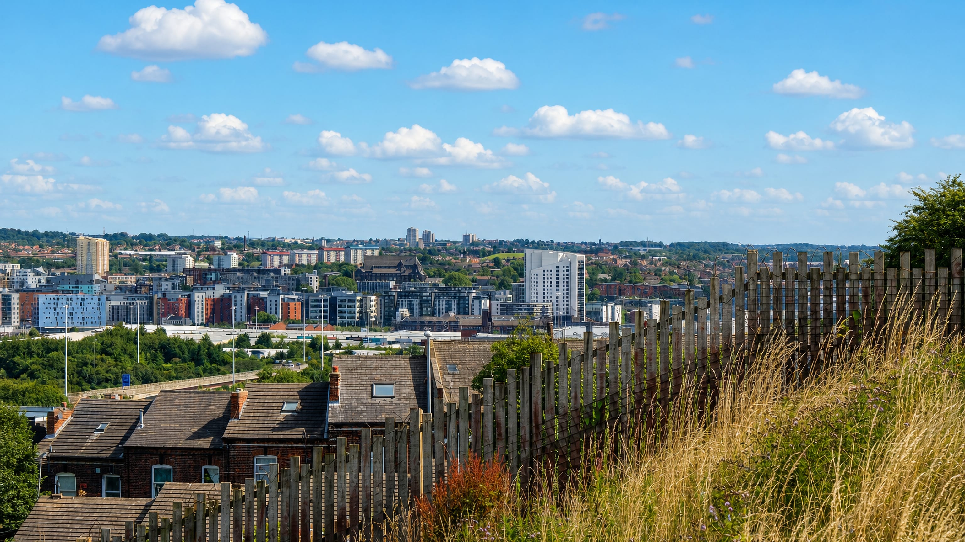 Leeds skyline of apartment towers and brick terraces seen across rooftops from a grassy hillside