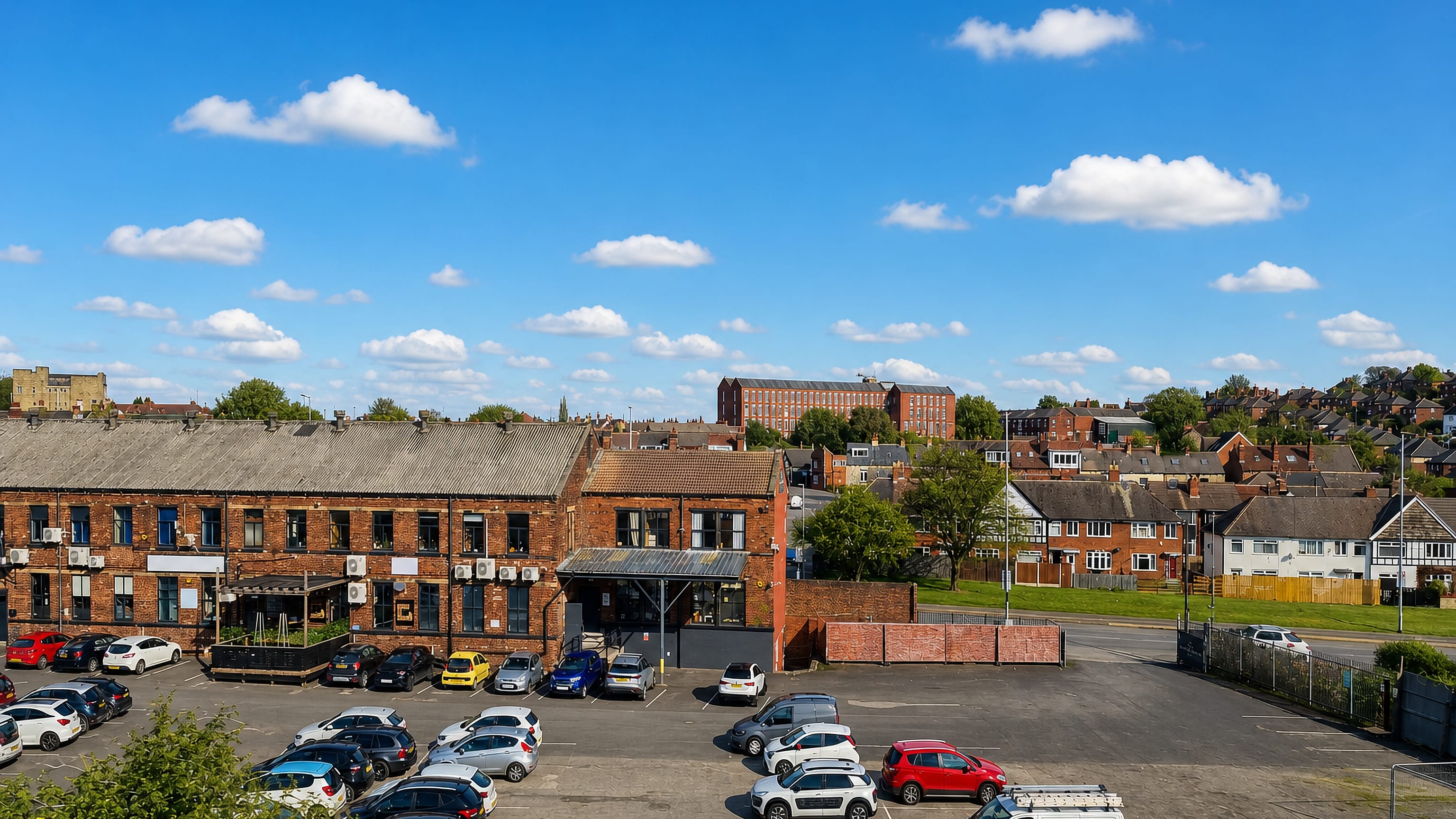Red-brick terraces, mill buildings and a car park under blue sky in Swinnow, Leeds.