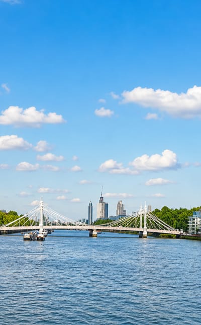 The River Thames at Battersea with a suspension bridge and modern riverside apartment blocks under a blue sky