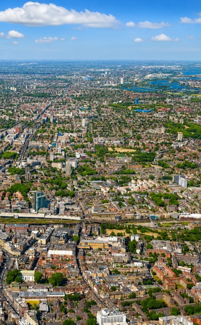 Aerial view over dense East London rooftops and green spaces toward the horizon at Bethnal Green.