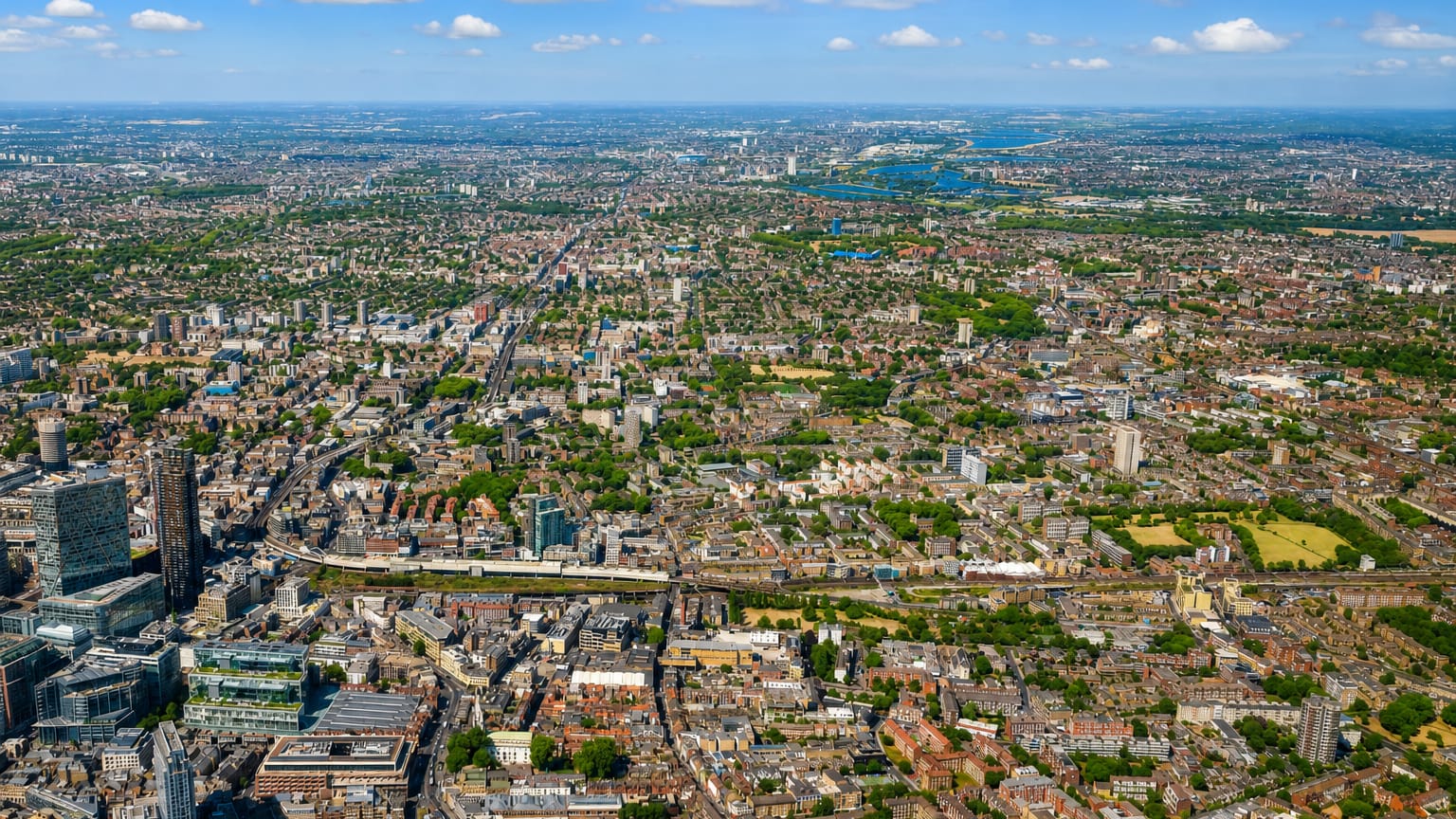 Aerial view over dense East London rooftops and green spaces toward the horizon at Bethnal Green.