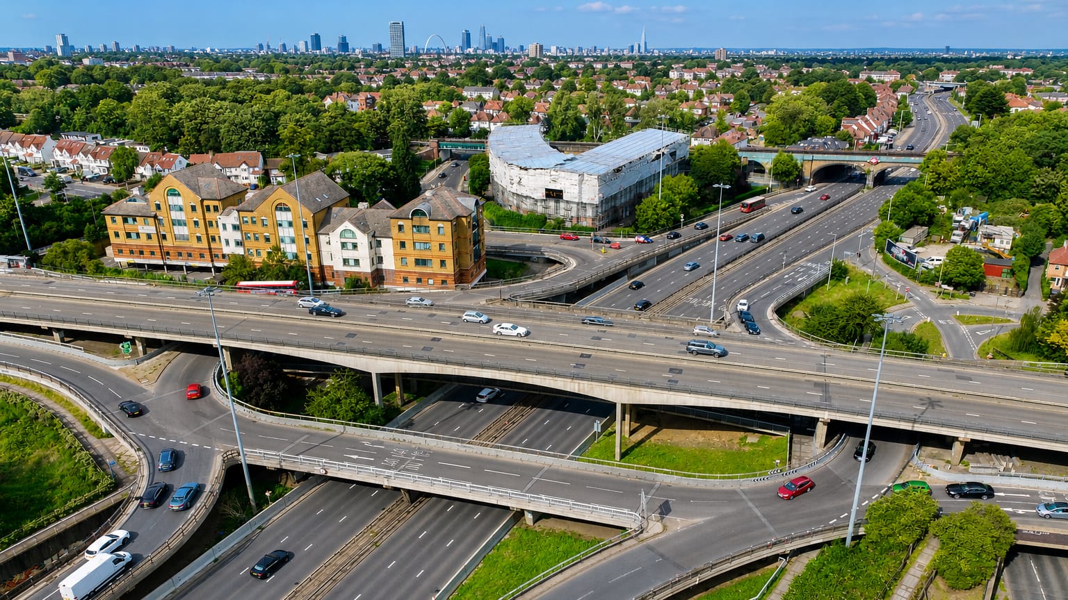 Aerial view of a multi-level road interchange and suburbs with the London skyline beyond, in Brent