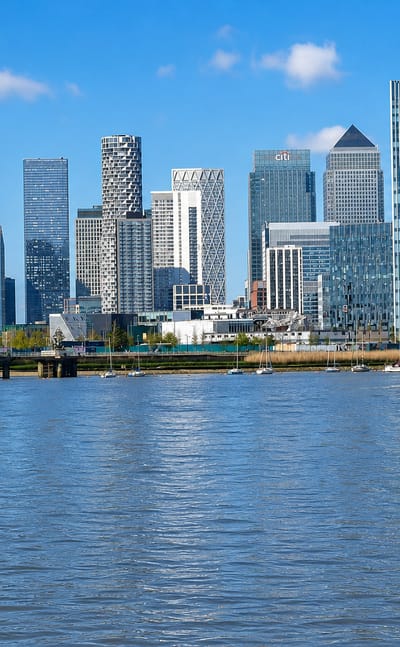 Canary Wharf's cluster of glass skyscrapers rising above the River Thames as boats pass, London.