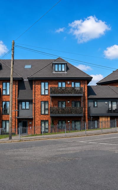 Modern red-brick apartment blocks at a road junction in Collier Row, London under a bright blue sky
