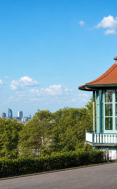 The ornate green bandstand in Horniman Gardens, Forest Hill, above treetops with London's skyline in the distance