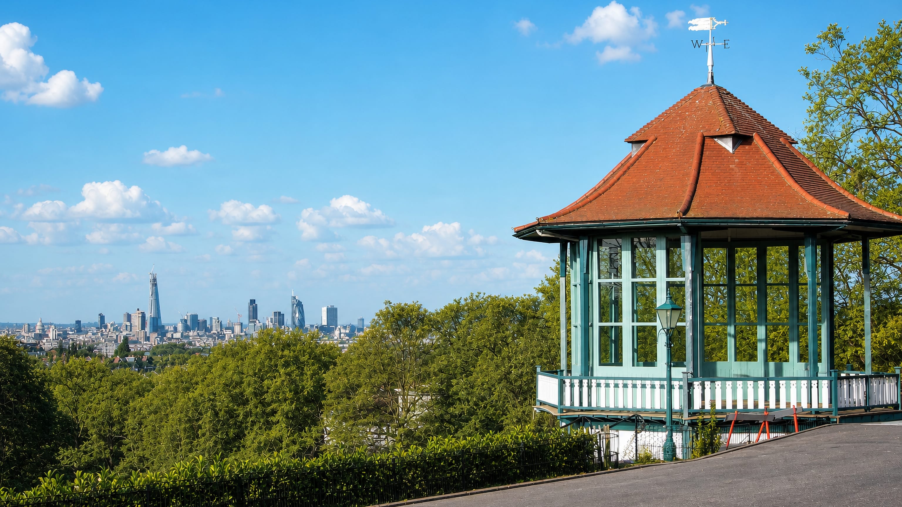 The ornate green bandstand in Horniman Gardens, Forest Hill, above treetops with London's skyline in the distance