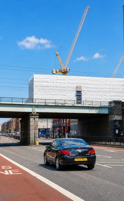 Traffic passing under a railway bridge on a red bus-lane road past a Costa cafe in Holloway, London.