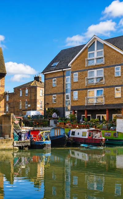 Canal-side brick apartments and moored narrowboats reflected in still water at Kensal Green, London.
