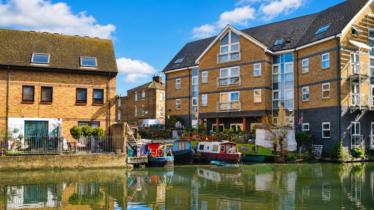 Canal-side brick apartments and moored narrowboats reflected in still water at Kensal Green, London.