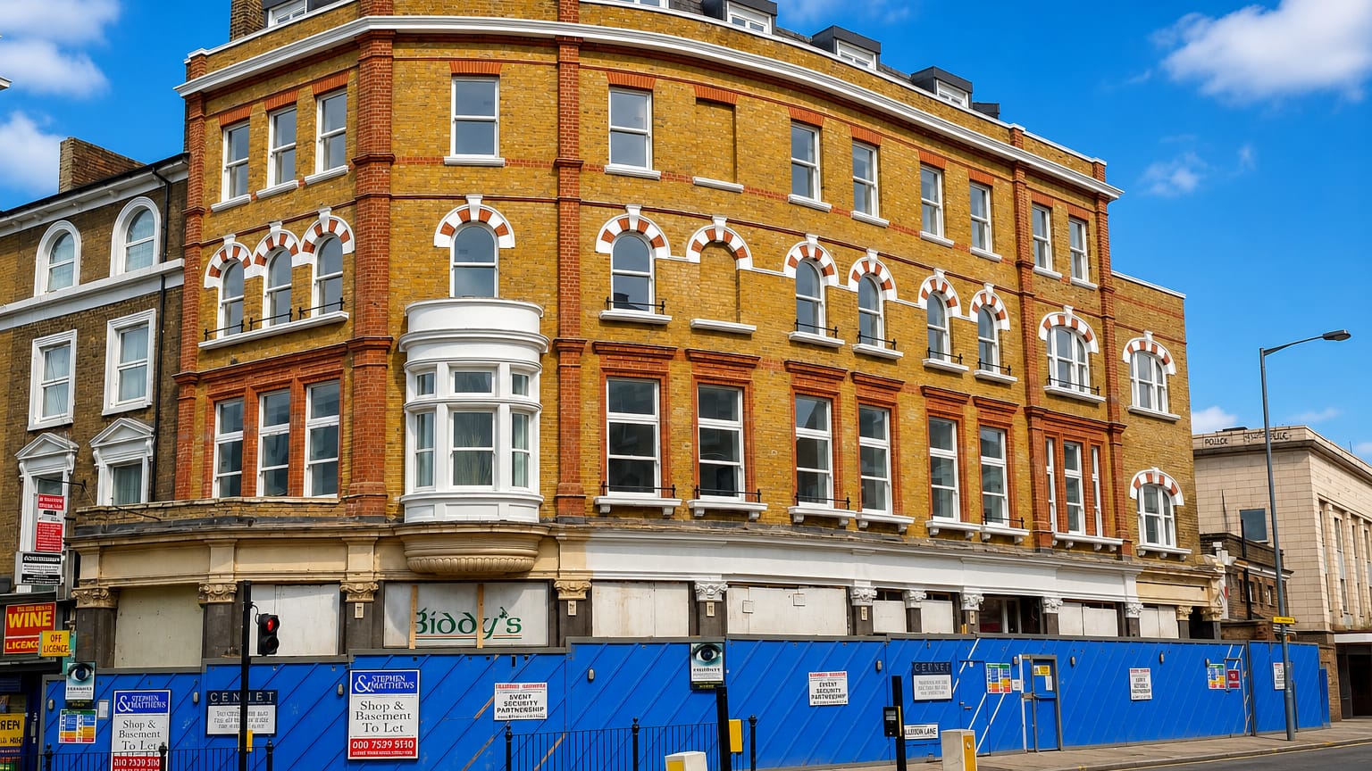 A yellow-brick Victorian corner building with shuttered shopfronts and to-let hoardings on a Kilburn street, London