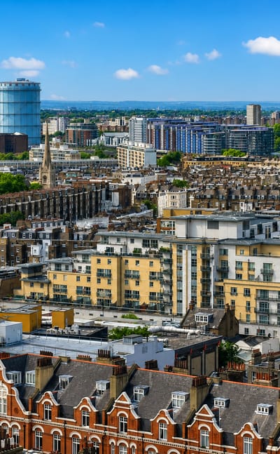Aerial view over Pimlico rooftops toward Battersea Power Station's white chimneys under a blue sky, London