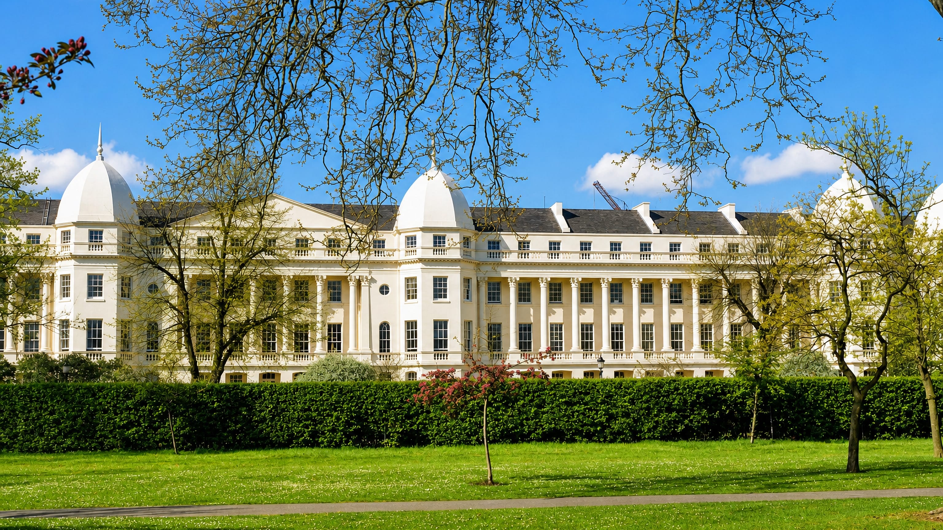 Cream Nash terrace with domed pavilions seen across the lawns and trees of Regent's Park in London