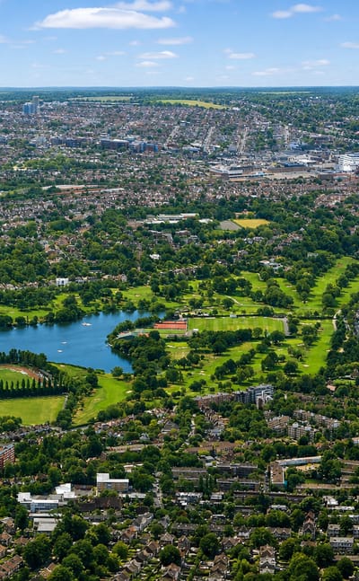 Aerial view over Wimbledon Park's lake and greenery toward the All England Lawn Tennis Club.
