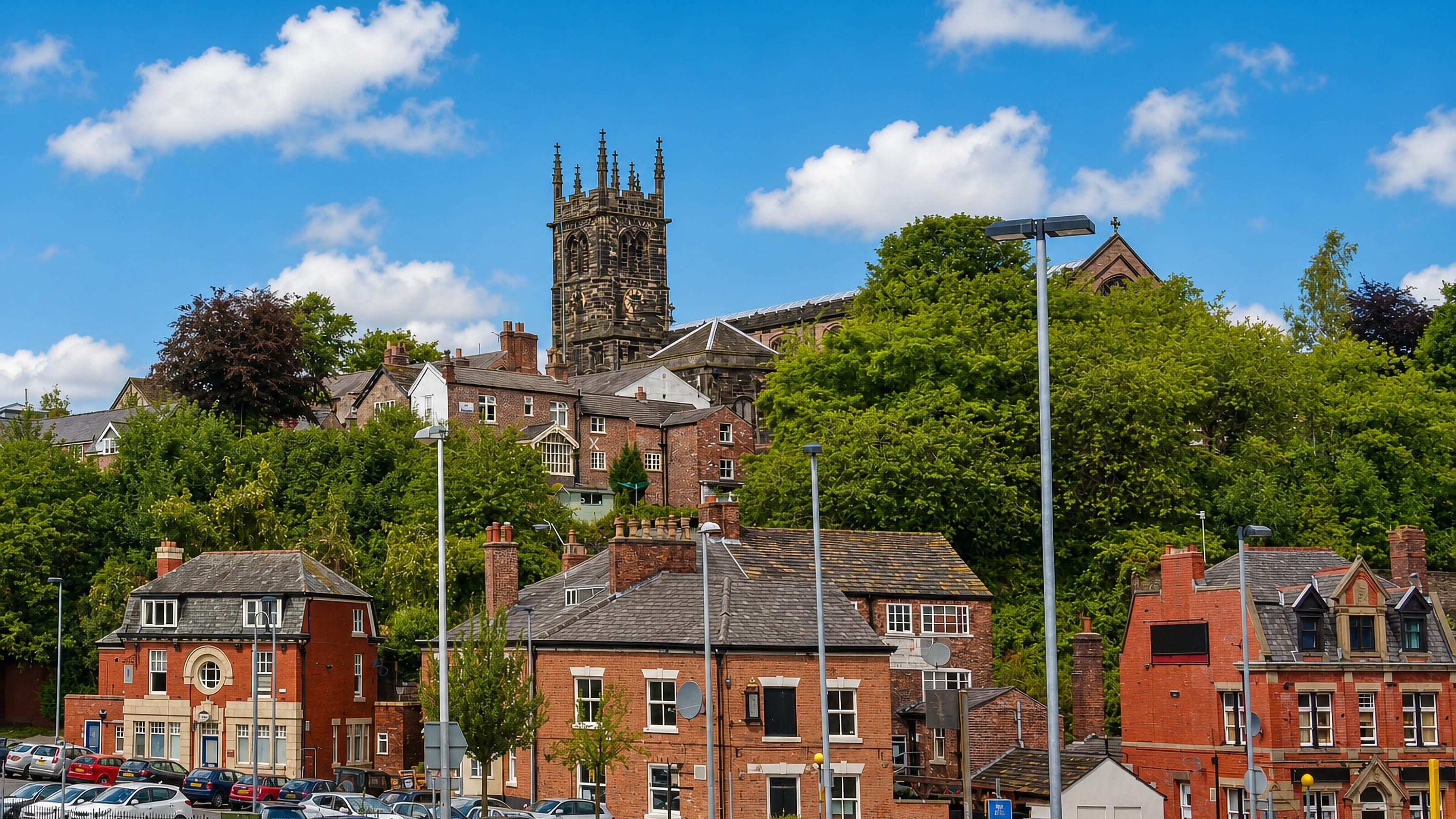 St Michael's church tower above red-brick terraces and wooded slopes in Macclesfield, Cheshire
