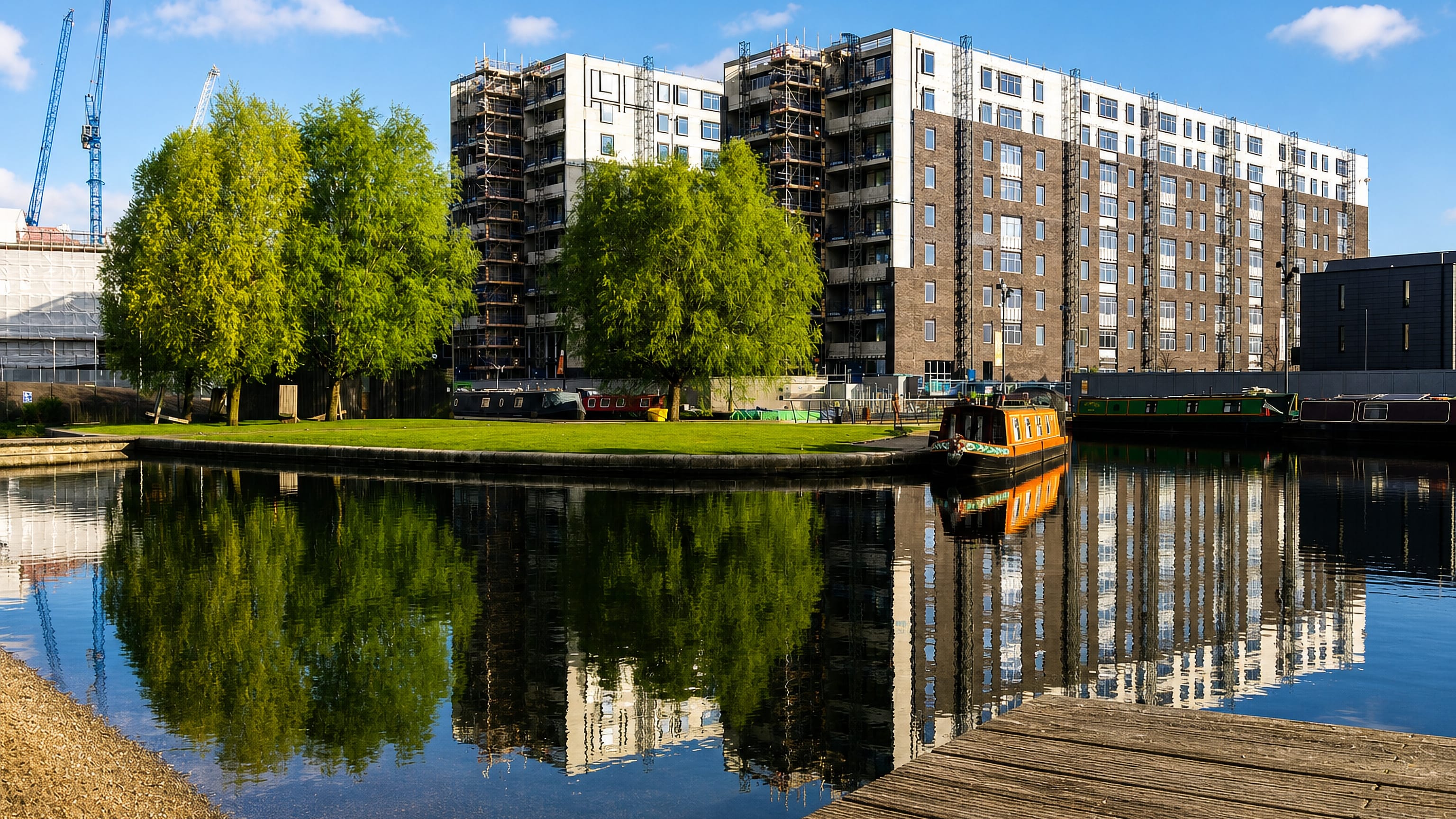 Narrowboats moored at the Ancoats canal basin in Manchester, below new brick and white apartment blocks under construction.
