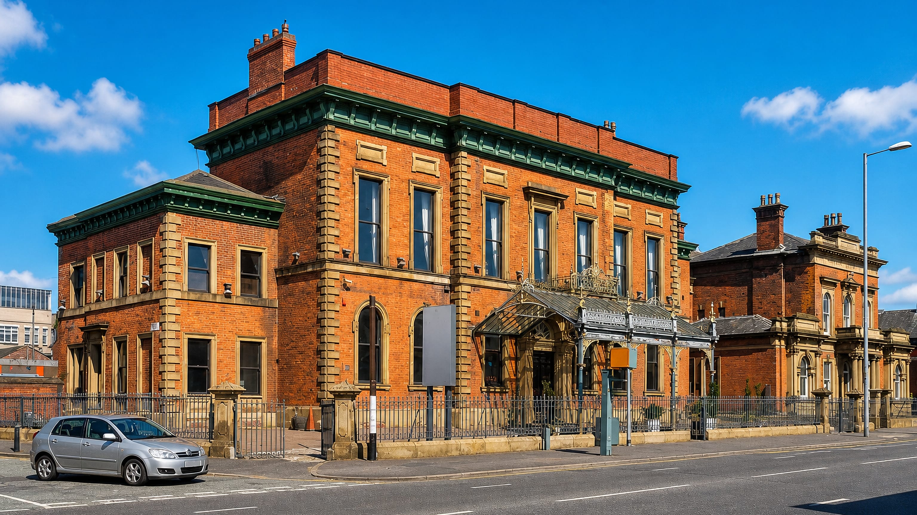 A Victorian red-brick building with an ornate cast-iron canopy on a main road in Cheetham Hill, Manchester.