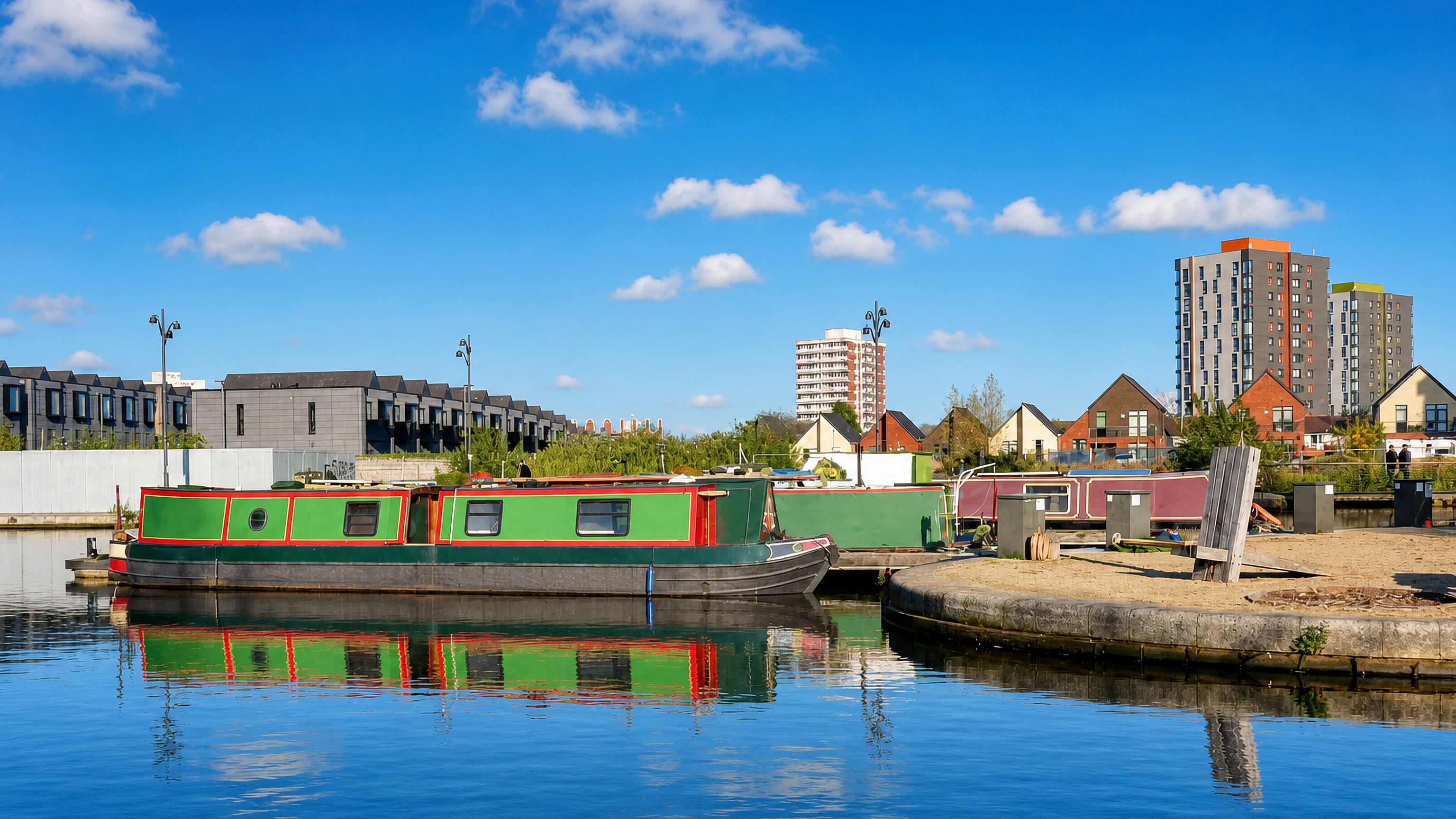 Narrowboats moored at New Islington Marina in Manchester, with new-build housing and a tower block behind.