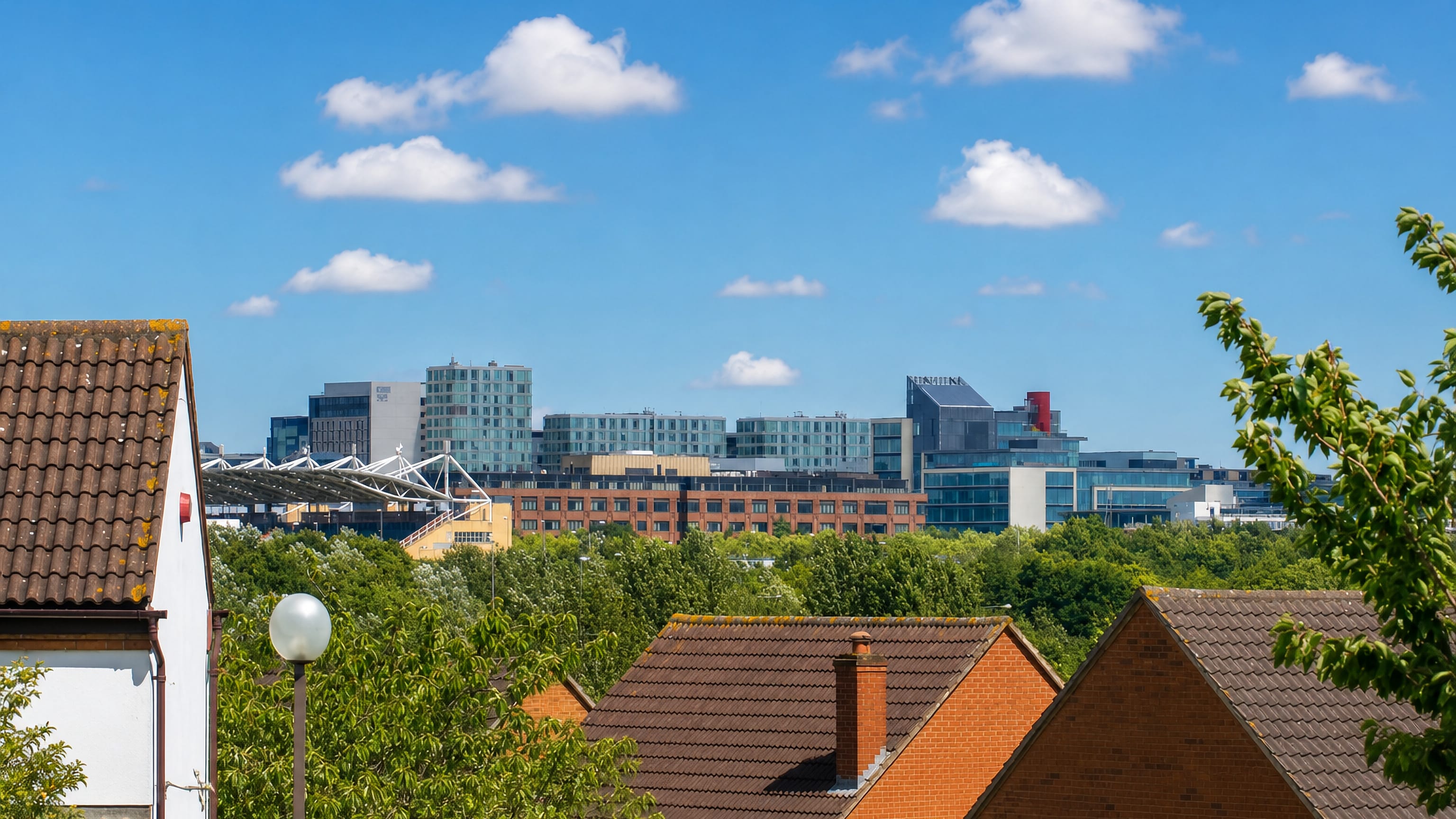 Glass-fronted offices of Central Milton Keynes rising beyond brick suburban rooftops and summer trees.