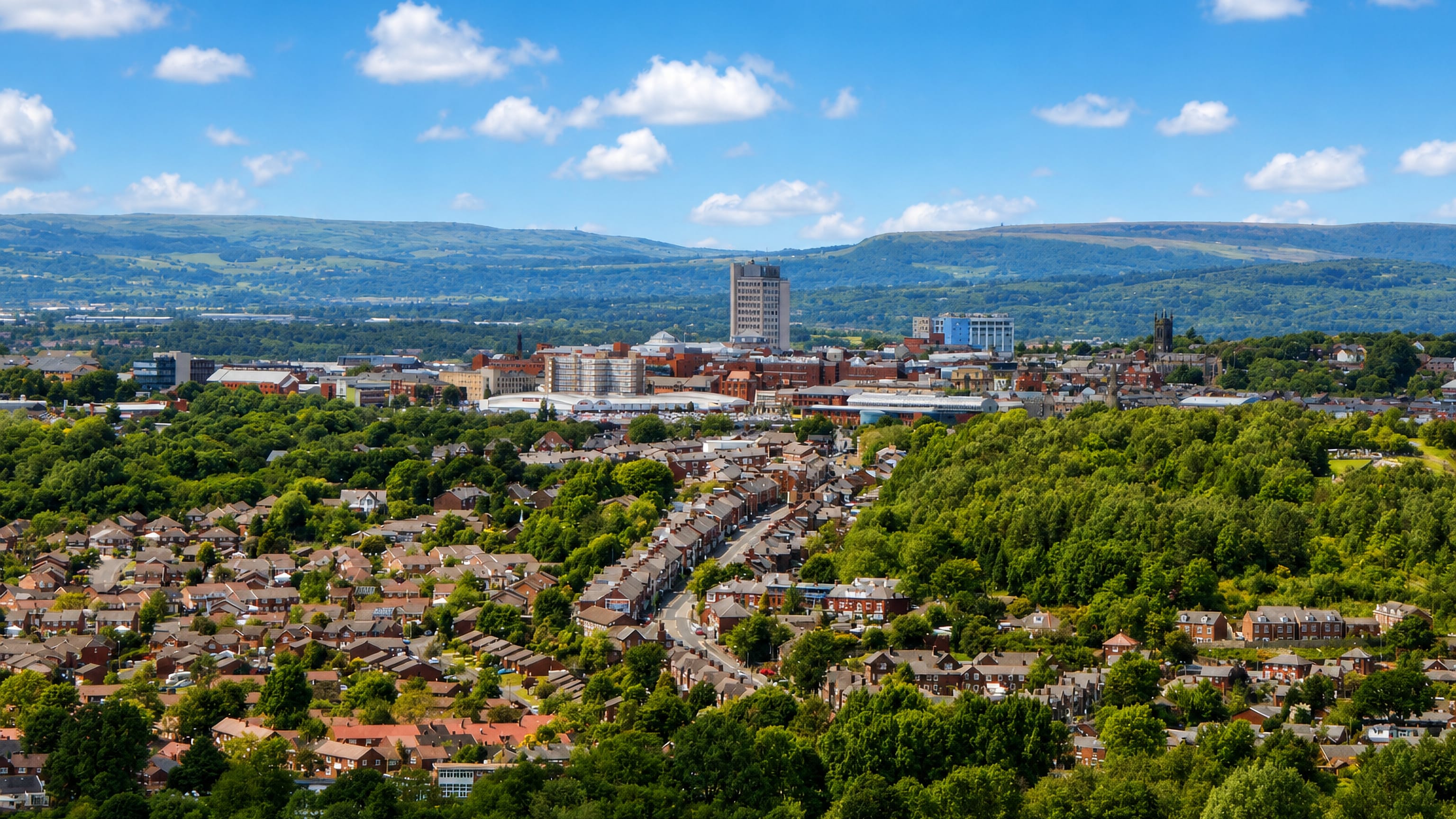 Oldham's terraced streets and town-centre tower blocks below the green Pennine moors, Greater Manchester.