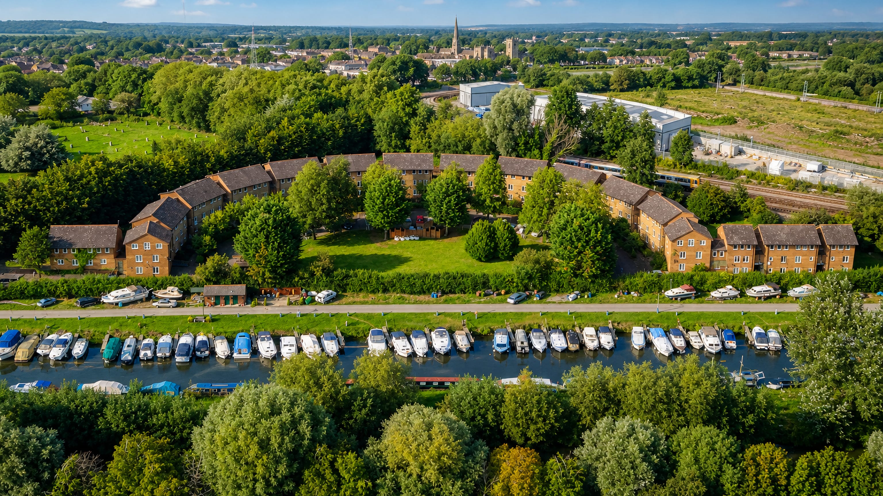 Aerial view of Osney in Oxford, curved brick housing beside a boat-lined Thames channel with city spires beyond.