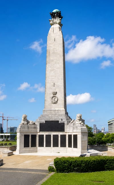 The Plymouth Naval Memorial obelisk stands on the green lawns of Plymouth Hoe under a clear sky.