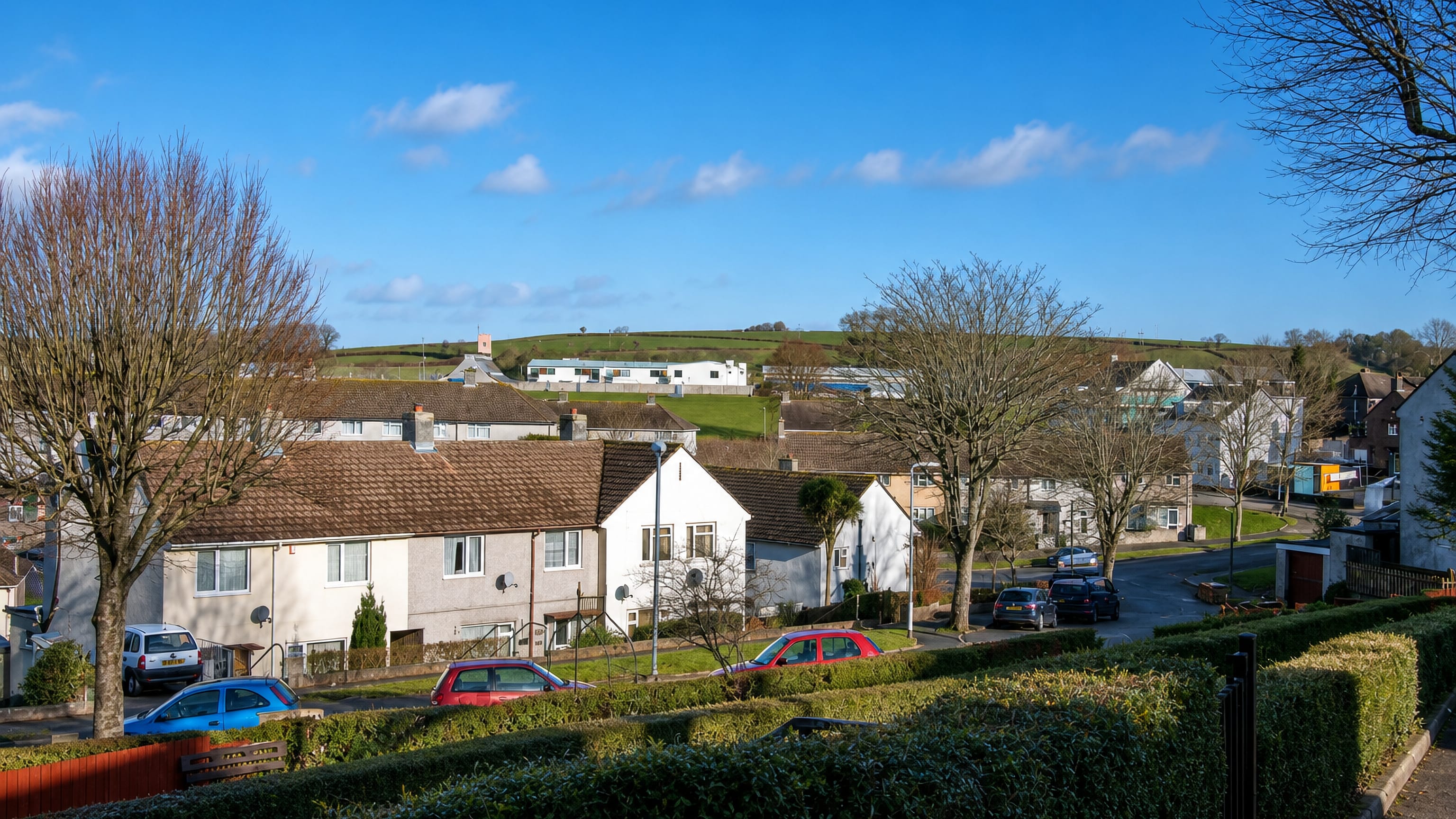 Postwar rendered houses and hedged gardens below green hills in Ernesettle, north-west Plymouth.