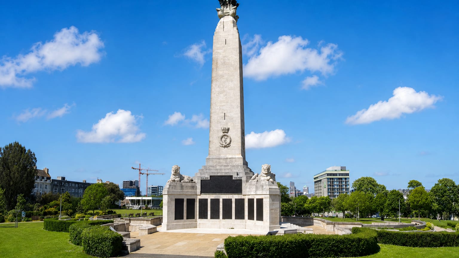 The Plymouth Naval Memorial obelisk stands on the green lawns of Plymouth Hoe under a clear sky.