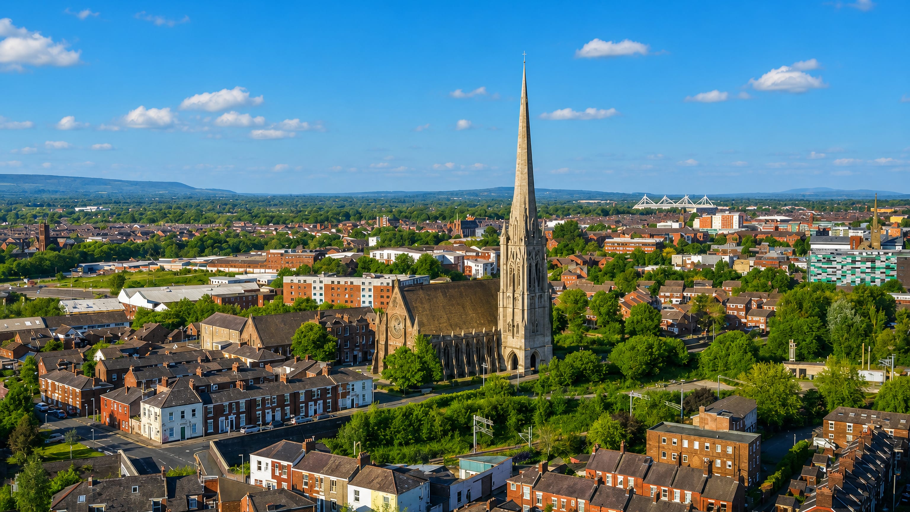 Aerial daytime view over Preston, England, with St Walburge's spire above red-brick terraced streets and distant hills.